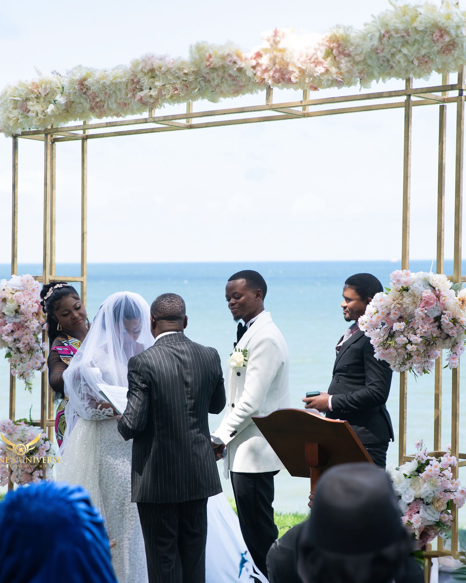 Couple exchanging vows beneath a floral arch by the water