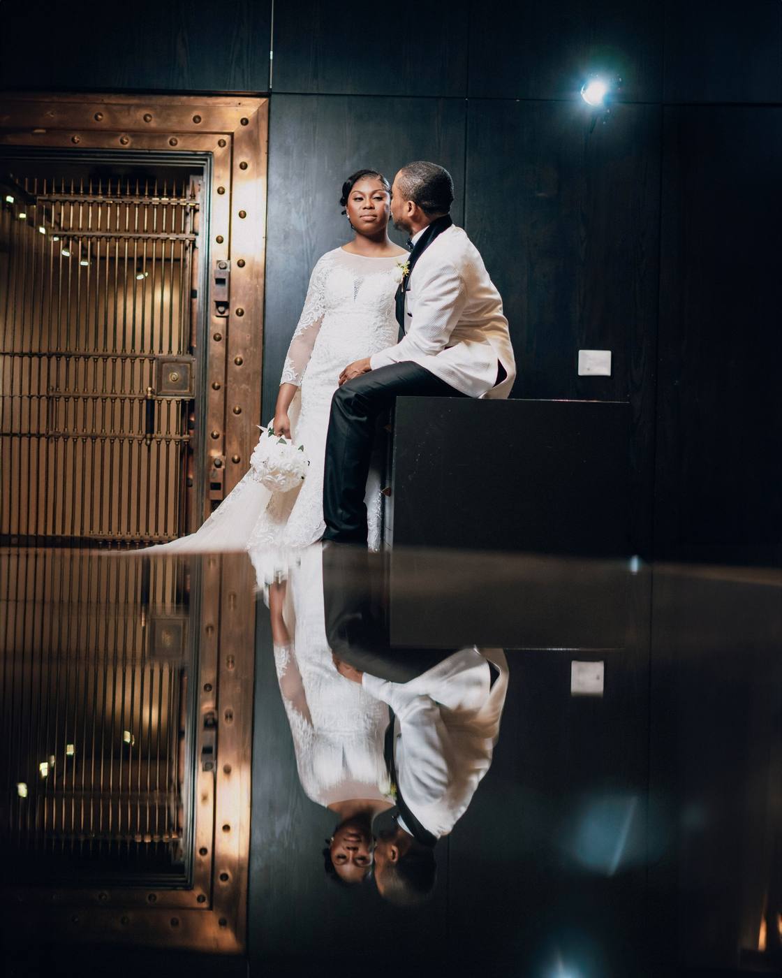 Bride and groom beside a brass bank vault door, reflected in a polished floor