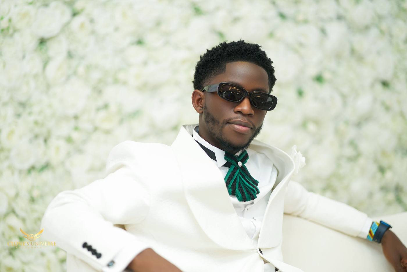 Groom in a white jacket and sunglasses against a white rose wall
